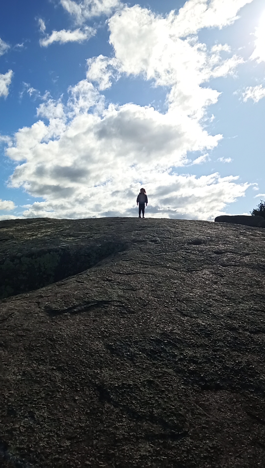 Silhouette of a person standing on top of a large rock trail